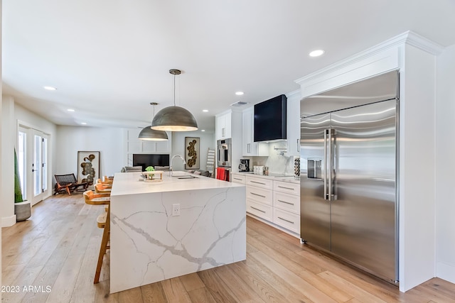 kitchen featuring a kitchen island with sink, sink, pendant lighting, stainless steel built in fridge, and white cabinetry