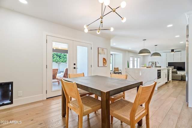 dining space with french doors, ceiling fan with notable chandelier, and light hardwood / wood-style flooring