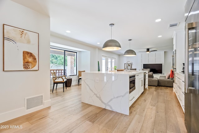 kitchen with pendant lighting, ceiling fan, light stone countertops, an island with sink, and white cabinetry