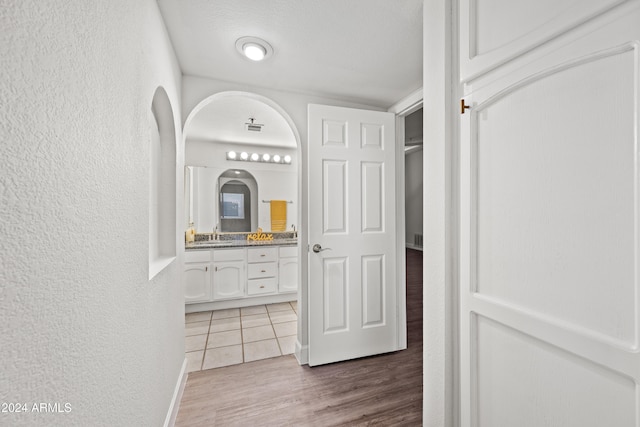 corridor with light wood-type flooring, a textured ceiling, and sink