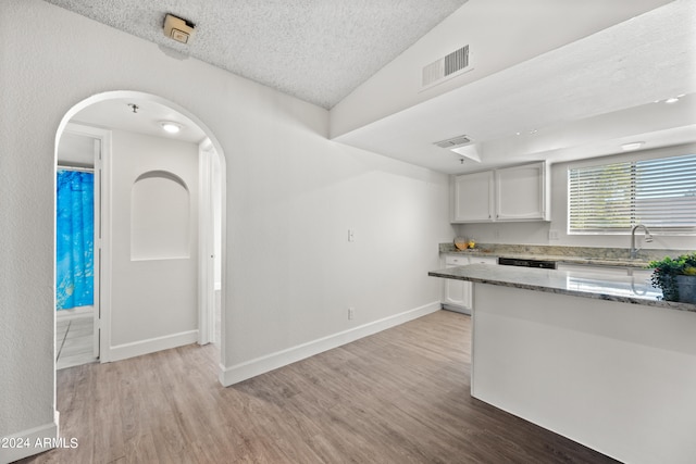 kitchen featuring light stone counters, light hardwood / wood-style floors, a textured ceiling, white cabinetry, and vaulted ceiling