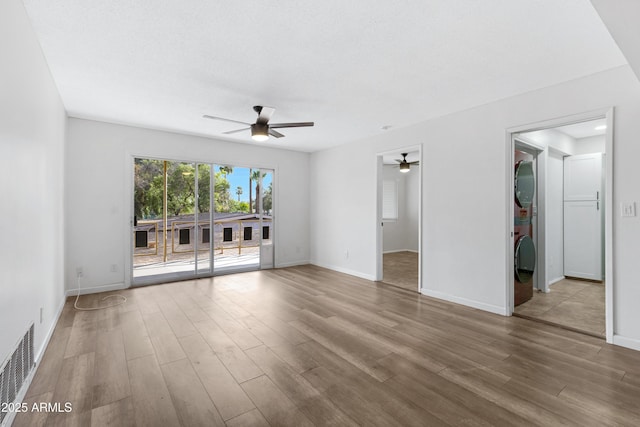 unfurnished living room with stacked washer / drying machine, ceiling fan, and light wood-type flooring