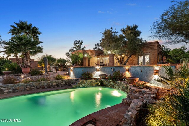 pool at dusk featuring pool water feature