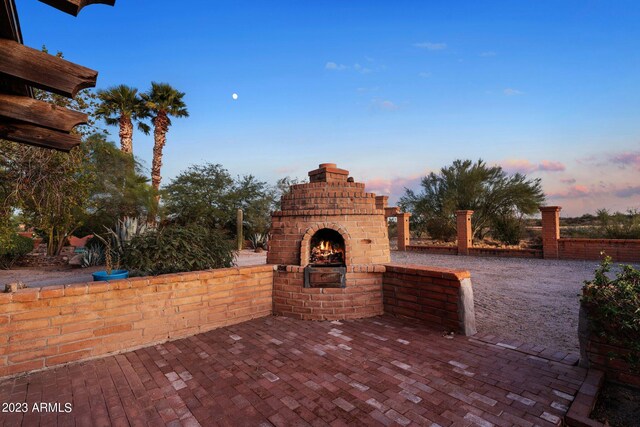 patio terrace at dusk featuring an outdoor brick fireplace