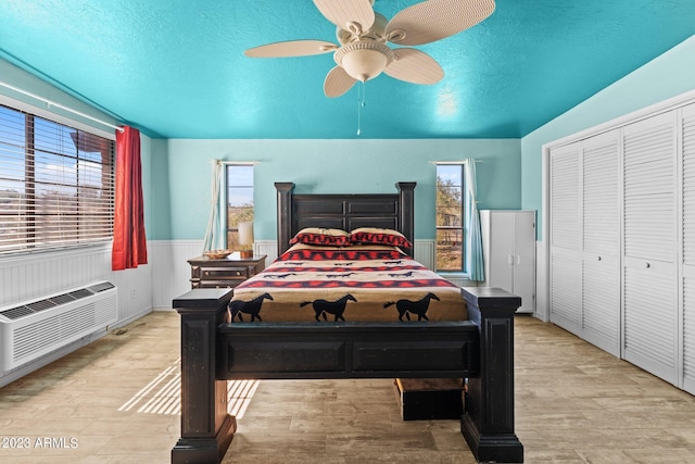 bedroom featuring a textured ceiling, ceiling fan, light wood-type flooring, and multiple windows