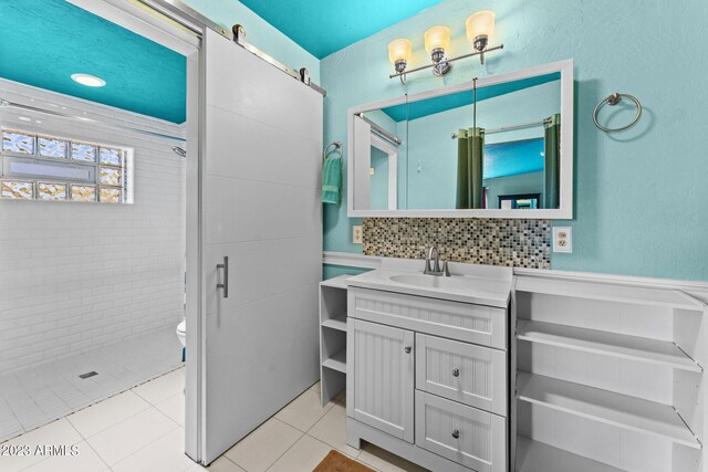 bathroom with toilet, tile patterned floors, vanity, tasteful backsplash, and tiled shower