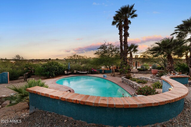 pool at dusk featuring a hot tub