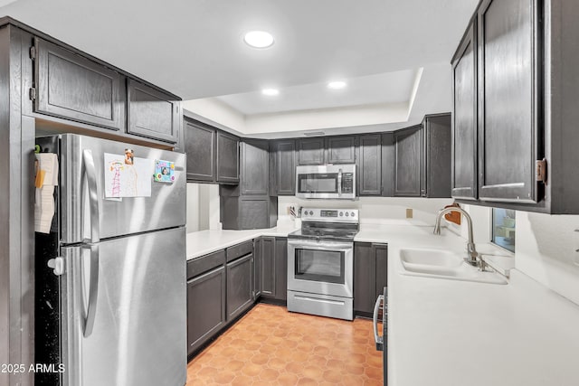 kitchen featuring light tile patterned flooring, appliances with stainless steel finishes, a tray ceiling, and sink