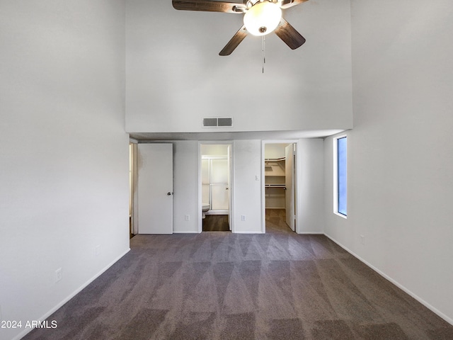 unfurnished bedroom with a towering ceiling, a walk in closet, dark carpet, ceiling fan, and a closet