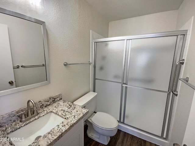 bathroom with hardwood / wood-style floors, vanity, toilet, and a shower with door