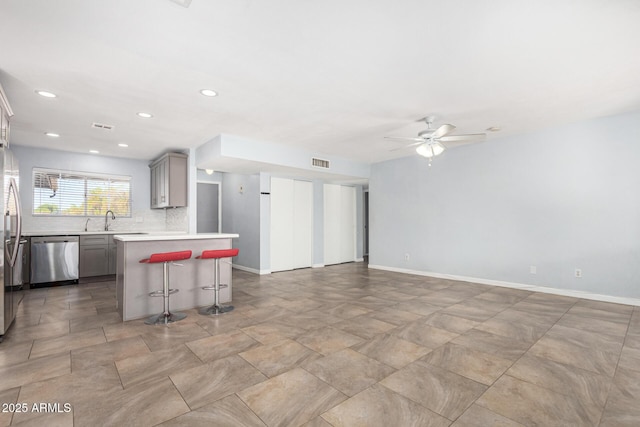 kitchen featuring sink, gray cabinets, a kitchen island, stainless steel appliances, and a kitchen bar