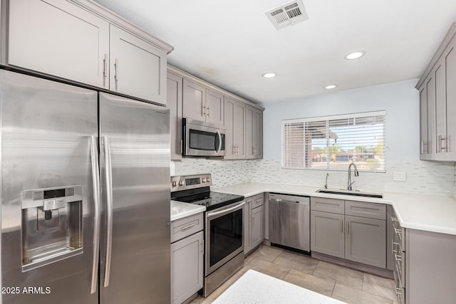 kitchen with sink, gray cabinetry, light tile patterned floors, appliances with stainless steel finishes, and backsplash