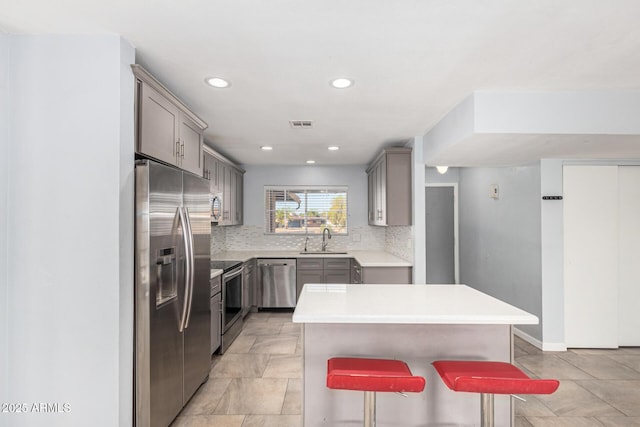 kitchen with a kitchen island, appliances with stainless steel finishes, sink, gray cabinetry, and a kitchen breakfast bar