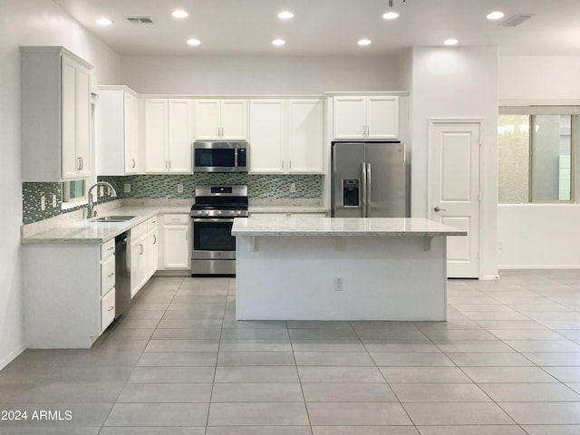 kitchen with light stone countertops, appliances with stainless steel finishes, sink, a center island, and white cabinetry