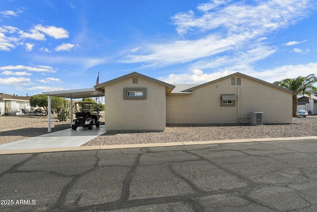 view of front of house featuring an attached carport, stucco siding, driveway, and central air condition unit