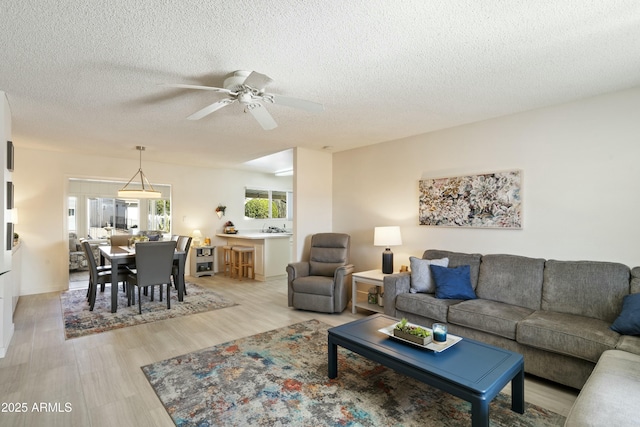 living room featuring ceiling fan, light wood-style flooring, and a textured ceiling