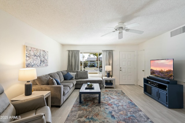 living area with a ceiling fan, light wood-type flooring, visible vents, and a textured ceiling