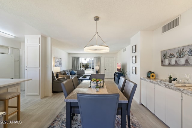 dining space with light wood-style flooring, visible vents, and a textured ceiling