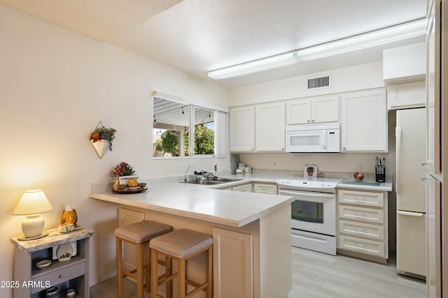 kitchen with white cabinets, a sink, white appliances, a peninsula, and a kitchen breakfast bar