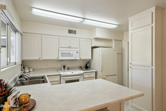 kitchen with a peninsula, white appliances, a sink, visible vents, and light countertops