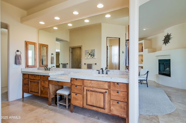 full bathroom featuring a sink, recessed lighting, a glass covered fireplace, and double vanity