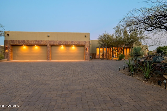 pueblo-style home with decorative driveway, a garage, and stucco siding