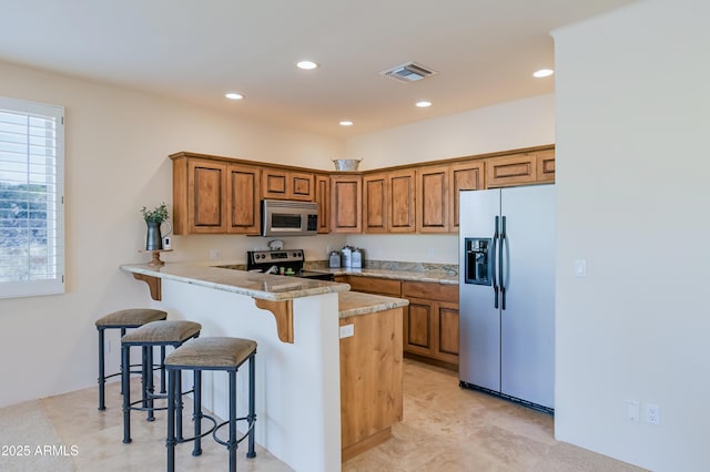 kitchen with visible vents, a peninsula, appliances with stainless steel finishes, a kitchen bar, and brown cabinets