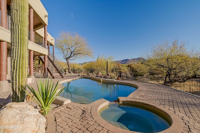 view of pool with a pool with connected hot tub, a patio, fence, stairway, and a mountain view