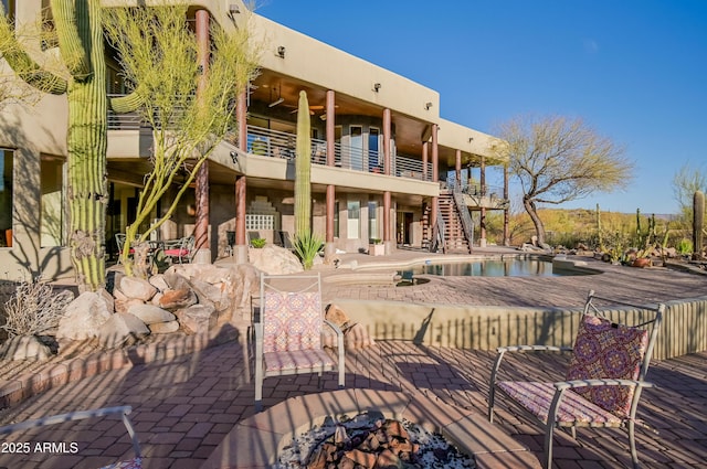 back of property featuring stairway, stucco siding, an outdoor pool, and a patio