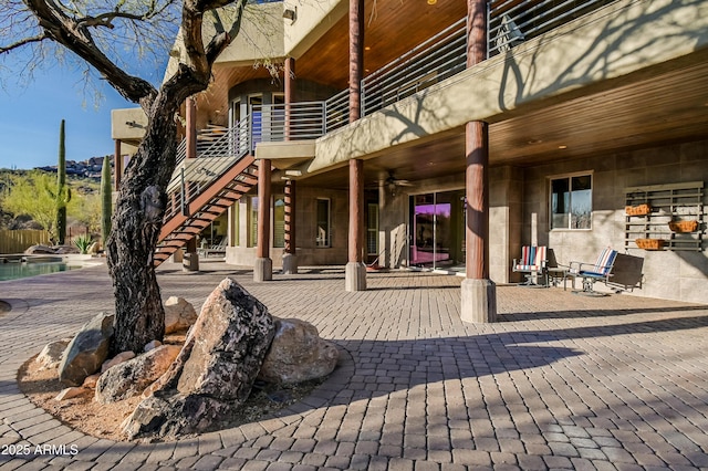 view of patio with a fenced in pool, a balcony, ceiling fan, and stairs