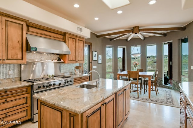 kitchen with visible vents, a sink, wall chimney exhaust hood, brown cabinetry, and high end range