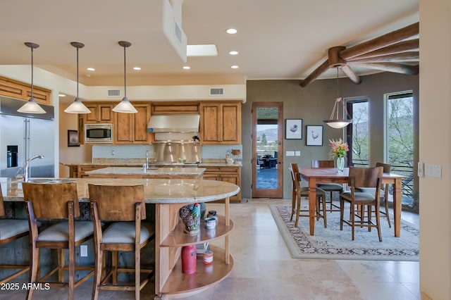 kitchen featuring built in appliances, a healthy amount of sunlight, wall chimney exhaust hood, and visible vents