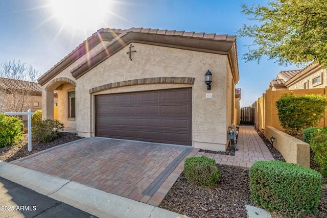 view of front of house featuring stucco siding, an attached garage, decorative driveway, and fence