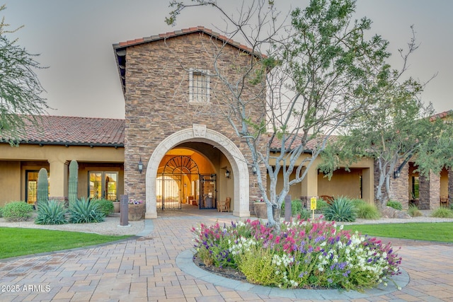 view of exterior entry with stucco siding, stone siding, and a tile roof