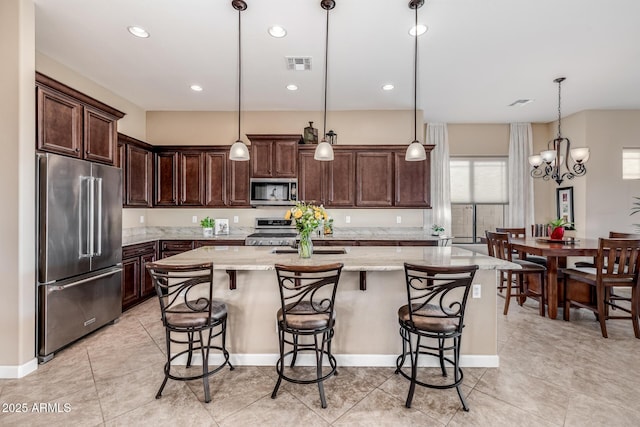 kitchen featuring visible vents, a center island with sink, stainless steel appliances, dark brown cabinetry, and light stone countertops