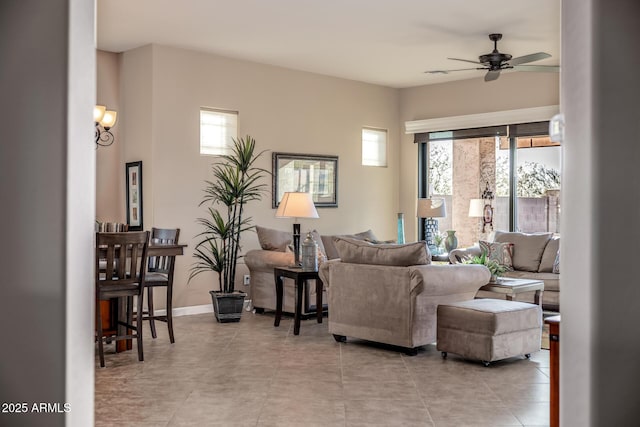 living area with light tile patterned floors, a ceiling fan, and baseboards