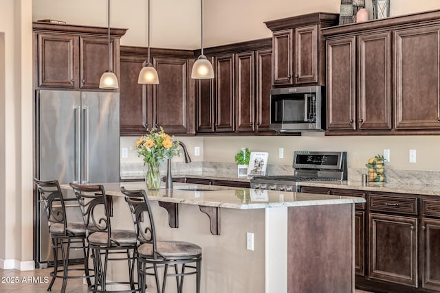 kitchen with dark brown cabinets, a breakfast bar area, an island with sink, appliances with stainless steel finishes, and a sink