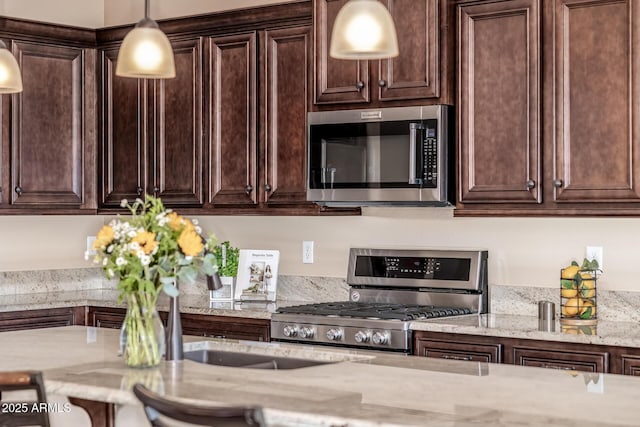 kitchen featuring light stone counters, stainless steel microwave, gas stove, dark brown cabinetry, and hanging light fixtures