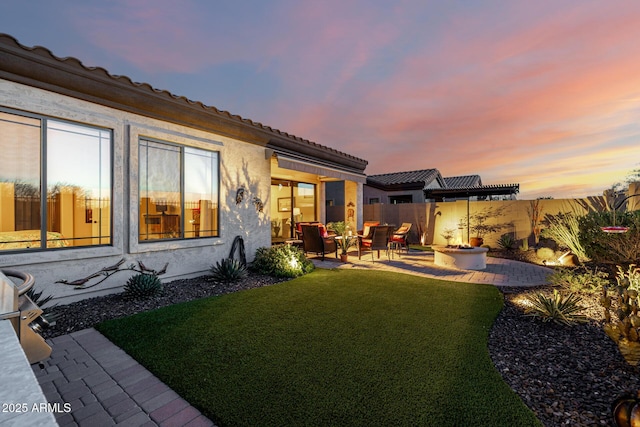 back of house at dusk featuring stucco siding, a patio, fence, a yard, and a fire pit