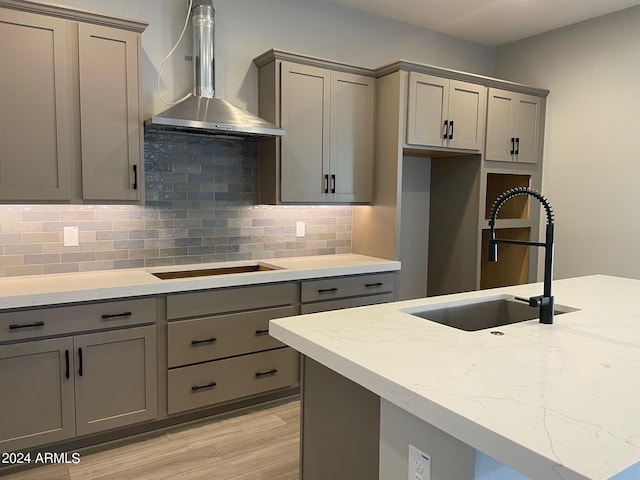 kitchen featuring gray cabinetry, sink, wall chimney range hood, light hardwood / wood-style flooring, and stovetop