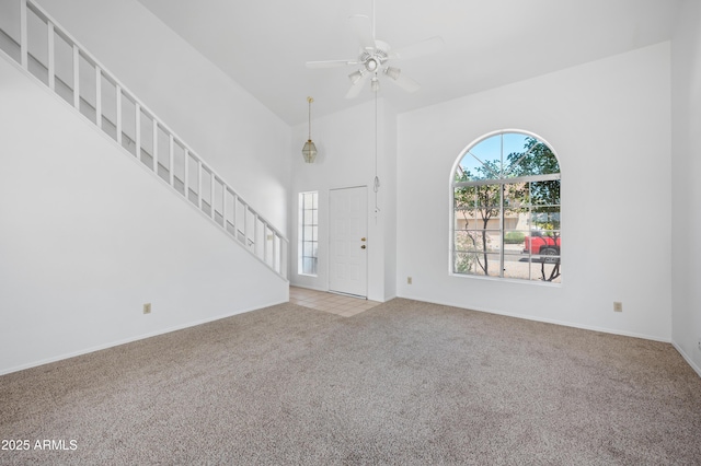 interior space with carpet, stairway, baseboards, a towering ceiling, and ceiling fan