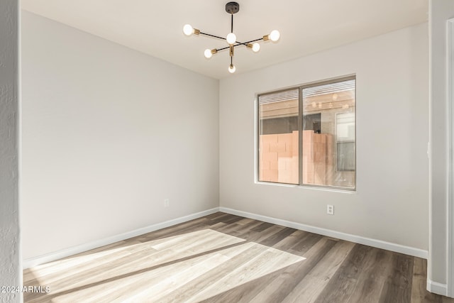 spare room with wood-type flooring and an inviting chandelier