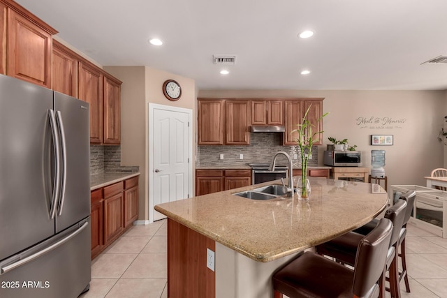 kitchen with sink, light tile patterned floors, appliances with stainless steel finishes, a kitchen breakfast bar, and an island with sink