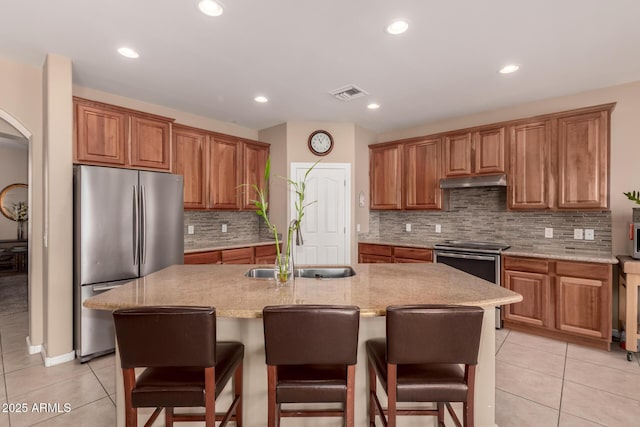 kitchen with appliances with stainless steel finishes, light stone countertops, a kitchen island with sink, and light tile patterned floors