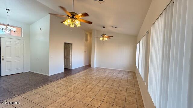 empty room featuring ceiling fan with notable chandelier, a wealth of natural light, and high vaulted ceiling