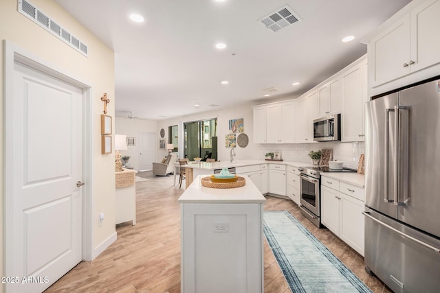 kitchen with light hardwood / wood-style flooring, backsplash, high end appliances, white cabinets, and kitchen peninsula