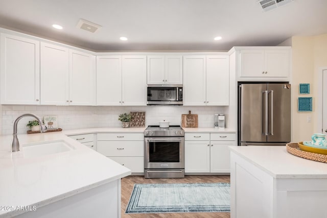 kitchen featuring high quality appliances, white cabinetry, sink, and decorative backsplash