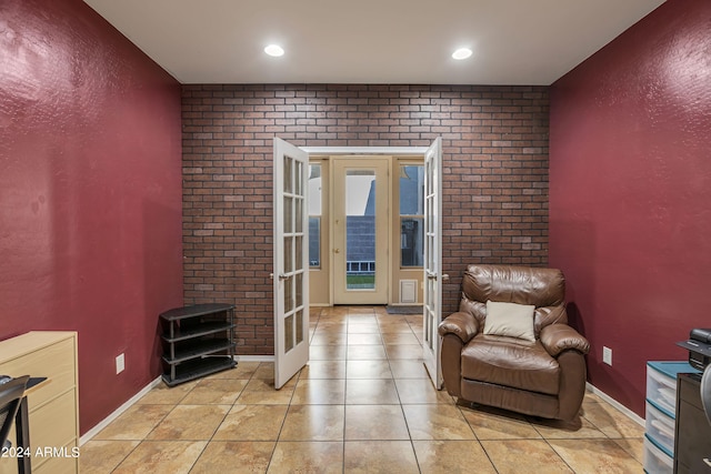 living area with french doors, light tile patterned floors, and brick wall