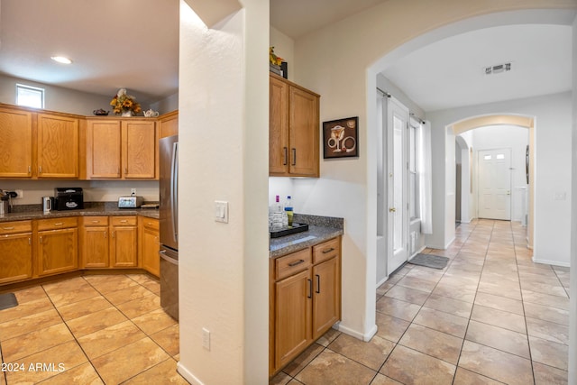 kitchen with dark stone counters, stainless steel fridge, and light tile patterned floors