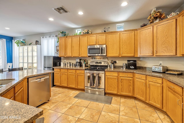 kitchen with appliances with stainless steel finishes, light stone counters, and light tile patterned floors